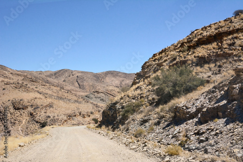 A dirt road in perspective between stone hills in the desert under a blue sky