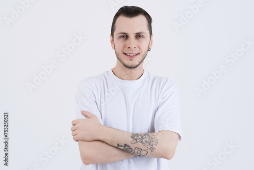 Portrait of attractive caucasian young man with tattoos in casual clothes with crossed arms isolated on white studio background. Confidently looking at the camera and smiling.