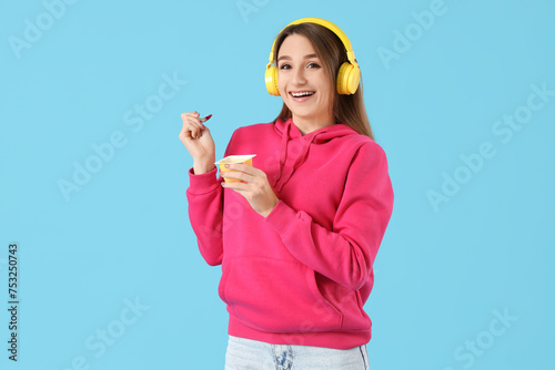 Young woman in headphones with tasty yoghurt on blue background