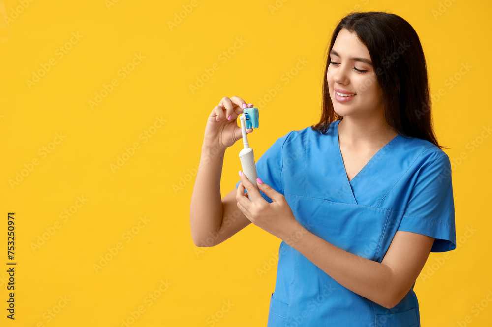 Female dentist with plastic tooth and electric toothbrush on yellow background. World Dentist Day Female dentist with plastic tooth and electric toothbrush on yellow background. World Dentist Day