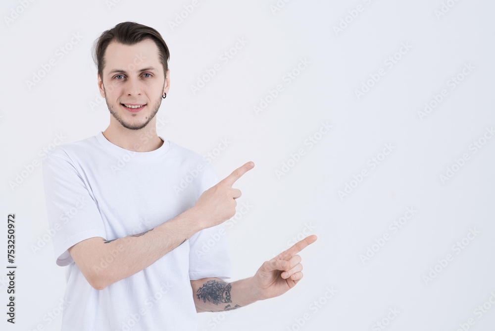 Attractive caucasian young man with tattoos in casual clothes smiling and pointing fingers at blank copy space for advertising isolated on white studio background Attractive caucasian young man with tattoos in casual clothes smiling and pointing fingers at blank copy space for advertising isolated on white studio background