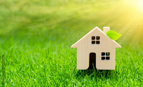 toy house model standing in green grass with a green leave, eco friendly concept, energy efficient solar powered housing