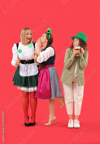 Women in costumes celebrating St. Patrick's Day on red background