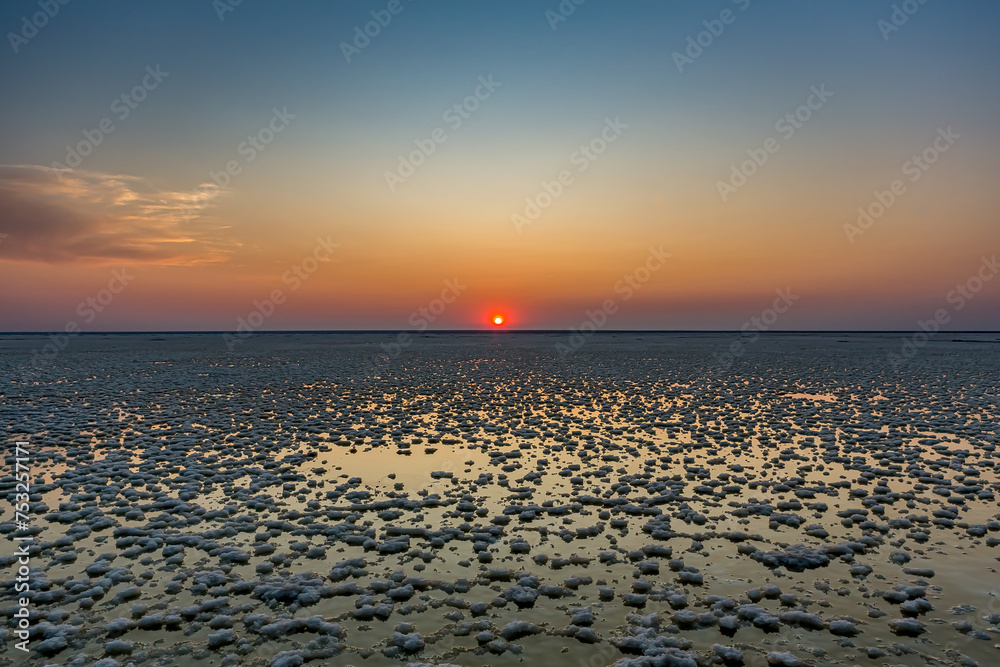 Sunset or sunrise on salt lake Elton (Russia) with mirror or reflection of low Cumulostratus or Stratocumulus clouds in the brine at golden hour with the sun in the background. Evening or morning.
