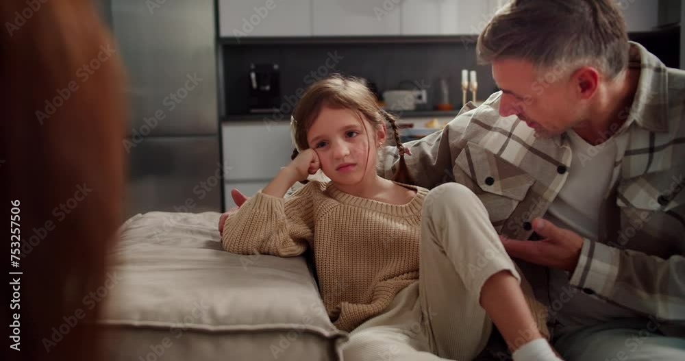 Sad and indignant little girl sits on the sofa and listens to her ...