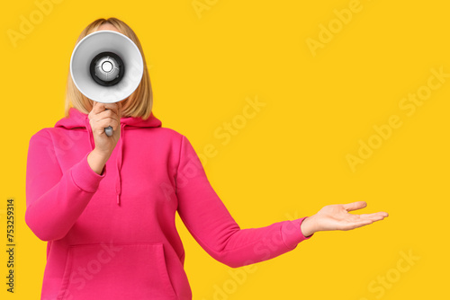Mature woman with megaphone pointing at something on yellow background
