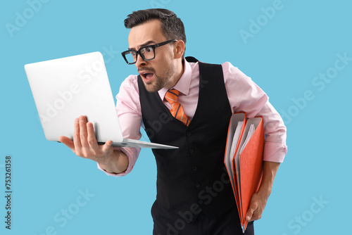 Funny shocked businessman with folders and laptop on blue background