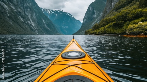 a yellow kayak is in the middle of a body of water with mountains in the background and a person standing on the front of the kayak. © Olga