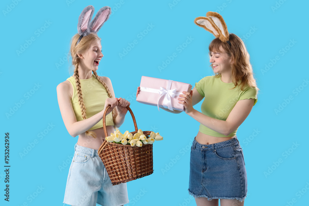 Young girls with Easter gift, basket and bunny ears on blue background Young girls with Easter gift, basket and bunny ears on blue background