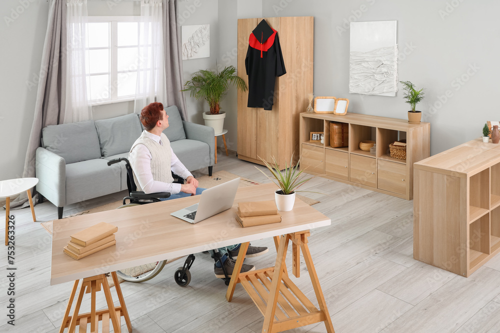 Male graduate in wheelchair with hanging robe at home