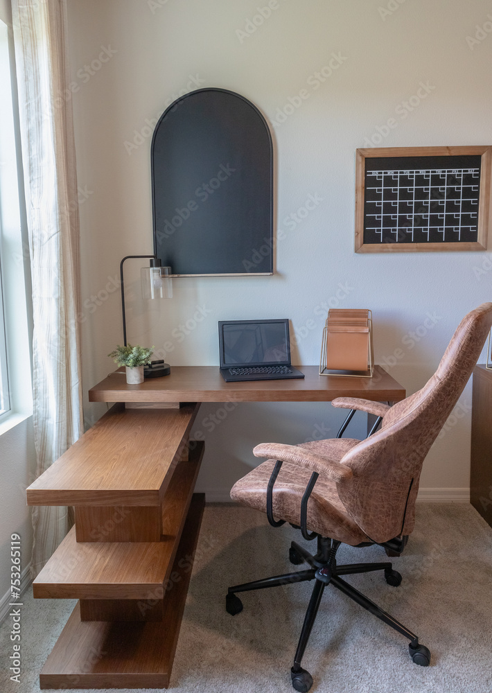 Fototapeta premium Vertical shot of home office with wood computer desk with leather chair in front of window