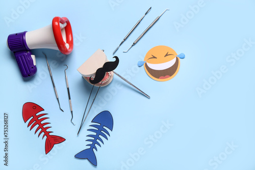 Megaphone with model of jaw, dentist tools and paper fishes on blue background. April Fools Day photo