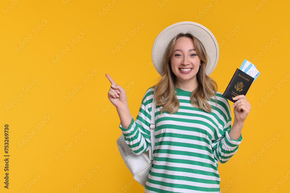 Happy young woman with passport, ticket and hat pointing at something on yellow background, space for text Happy young woman with passport, ticket and hat pointing at something on yellow background, space for text
