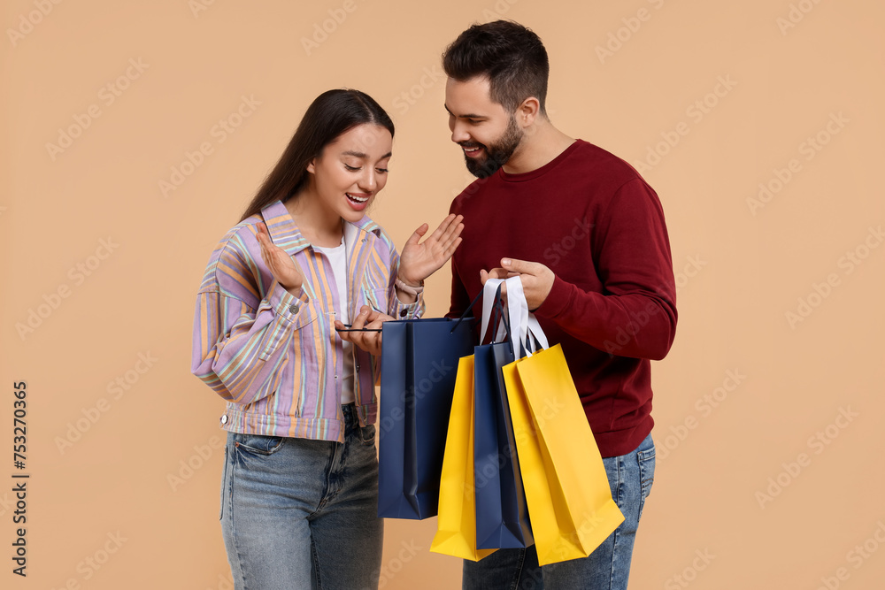 Man showing shopping bag with purchase to his girlfriend on beige background Man showing shopping bag with purchase to his girlfriend on beige background