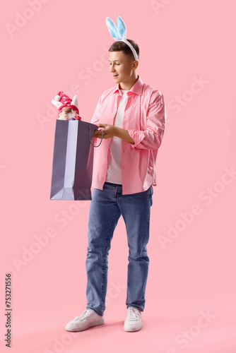 Young man in bunny ears with gnome and shopping bag on pink background. Easter Sale