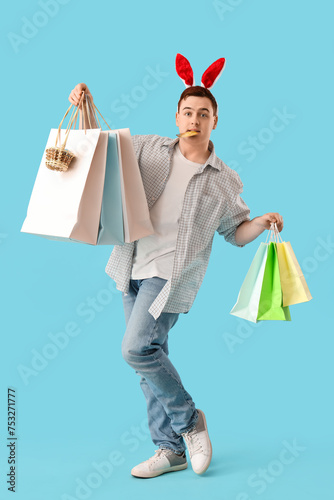 Young man in bunny ears with credit card and shopping bags on blue background. Easter Sale