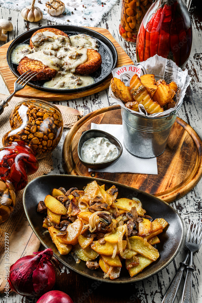 Different dishes from potatoes, fried potato pancakes, homemade potatoes with mushrooms and french fries potatoes in craft paper on wooden background, top view