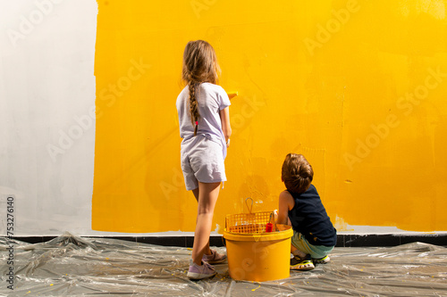 A boy and a girl paints a wall at home in yellow photo
