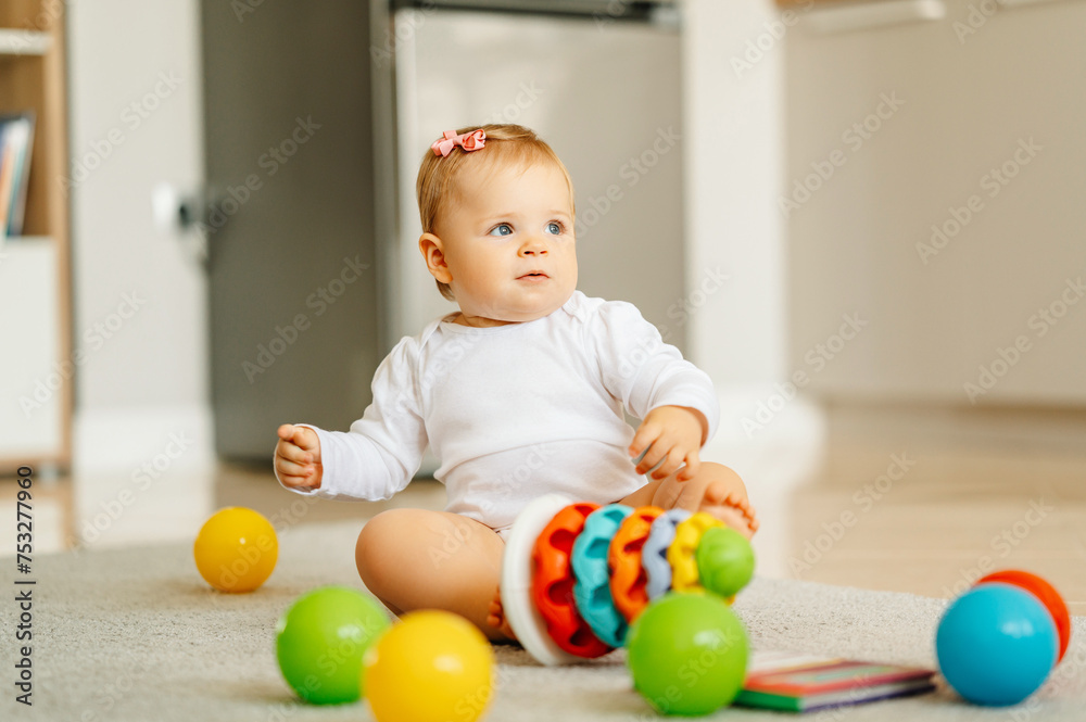 Cute sitting on the floor little baby girl is playing with colourful toys at home. Cute sitting on the floor little baby girl is playing with colourful toys at home.