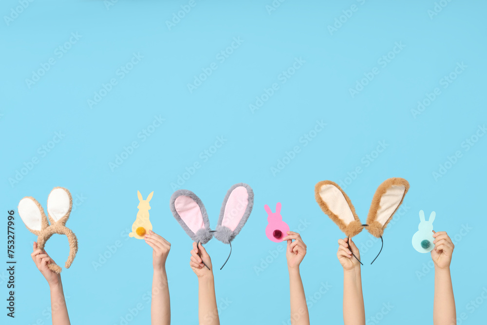 Female hands holding Easter bunny ears headbands and paper rabbits on blue background