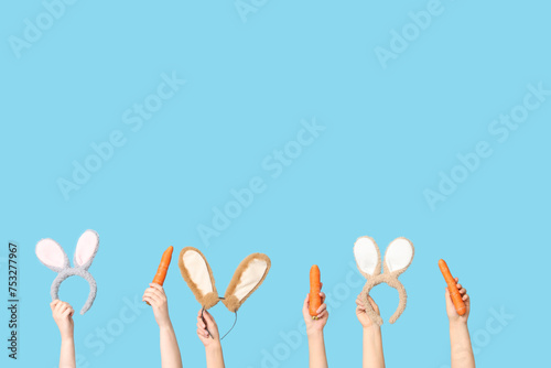 Female hands holding Easter bunny ears headbands and carrots on blue background