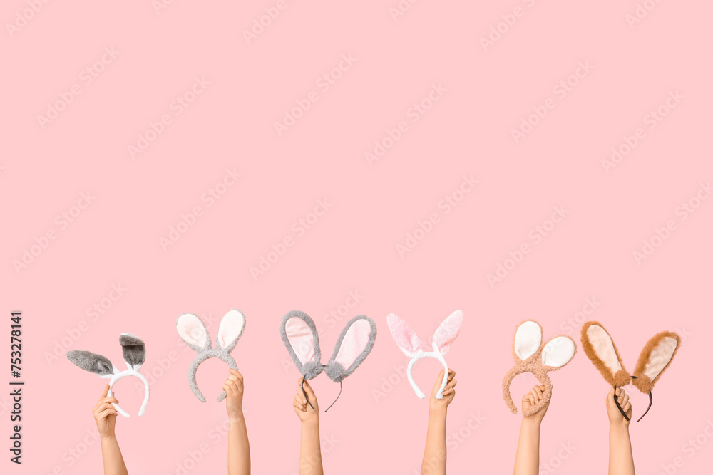 Female hands holding Easter bunny ears headbands on pink background
