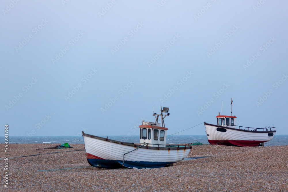 Two fishing boats on a shingle beach along the British coast, Image shows a fishing boat in good condition grounded on the beach ready to go out to sea