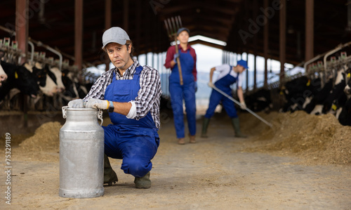 Focused male farm worker carrying big milk can walking in cowshed on dairy farm