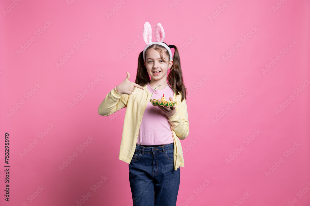On a pink backdrop, cute small girl grabs an arrangement of eggs and a chick as Easter items. Little one portraying excitement at the idea of spring celebrations and youth, bunny ears. On a pink backdrop, cute small girl grabs an arrangement of eggs and a chick as Easter items. Little one portraying excitement at the idea of spring celebrations and youth, bunny ears.