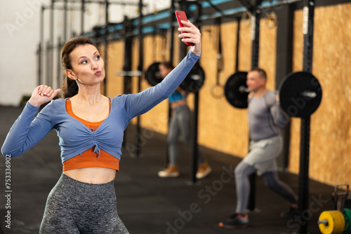 Smiling charismatic athletic woman take selfies with his smartphone after hard workout in modern cross fitness class