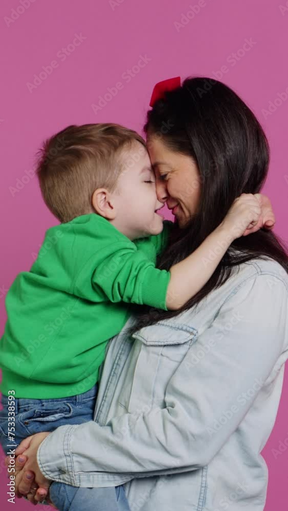 Vertical Video Adorable small boy hugging his mother and playing around, having fun against pink background. Young toddler posing with his mom holding him, laughing and being cheery. Camera A. Vertical Video Adorable small boy hugging his mother and playing around, having fun against pink background. Young toddler posing with his mom holding him, laughing and being cheery. Camera A.