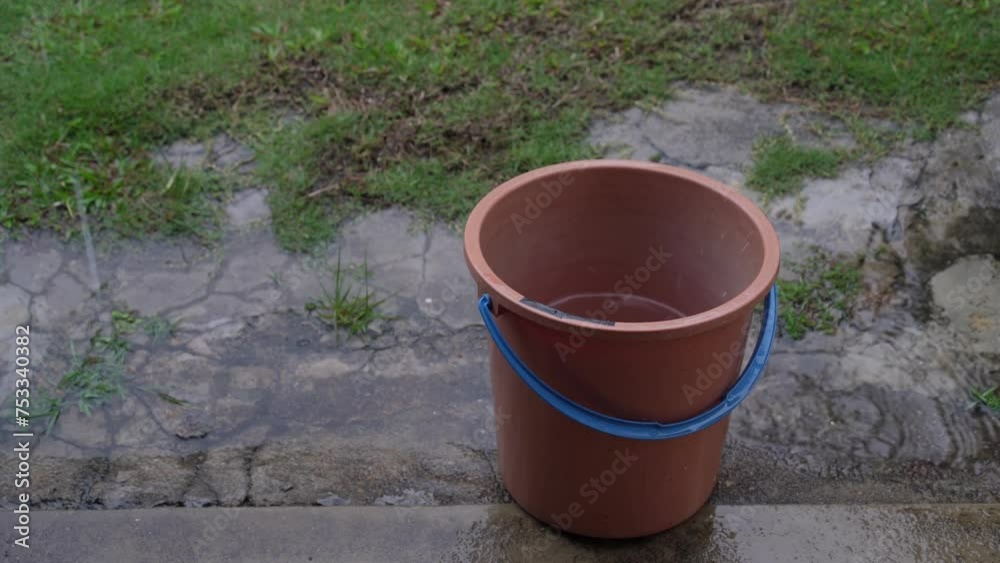 Rain water falling from the roof into the red bucket to save water. Rain water falling from the roof into the red bucket to save water.