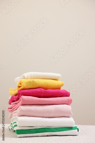 Stack of folded clothes on wooden table against beige background, space for text