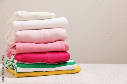 Stack of folded clothes on wooden table against grey background, space for text