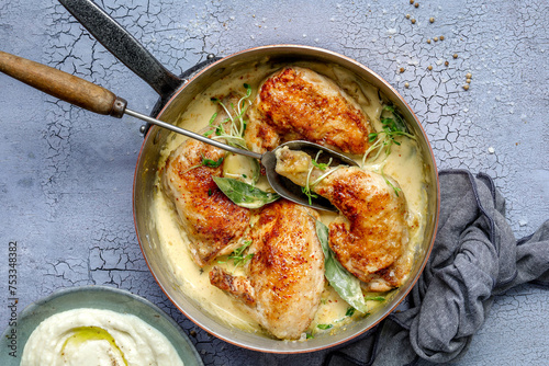 Braised pieces of chicken with dijon mustard sauce in a copper pan with herb garnish on light, grey background, landscape style, overhead shot with grey tea towel and a side of mash photo