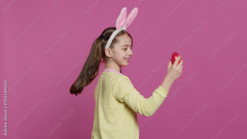 Enthusiastic small child spinning around in front of camera, presenting her red painted egg for easter sunday festivity. Cheery toddler with bunny ears twirling and doing a pirouette. Camera A. Enthusiastic small child spinning around in front of camera, presenting her red painted egg for easter sunday festivity. Cheery toddler with bunny ears twirling and doing a pirouette. Camera A.