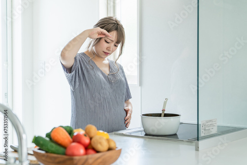 妊娠中にキッチンで調理中に体調不良になる女性（頭痛・発熱）
 photo