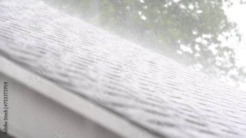 Panning shot of torrential downpour of rain on an asphalt roof.
