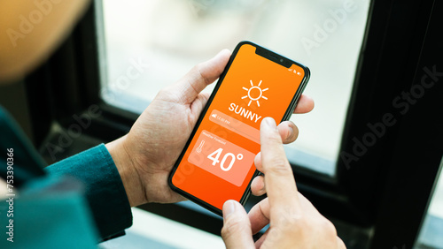  Hand holding smartphone with weather hot sunny day on screen and sunrise on midday at dry forest background. High Temperature Weather show on Mobile Screen on Hot Sunny Day. concept global warming photo