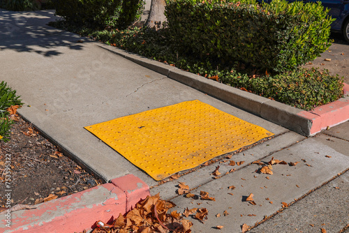 Close-up of disabled sidewalk entry, yellow tactile with a disabled sign to support wheelchair disabled people. Bright yellow tactile paving for blind pedestrians. Guiding block for disability.