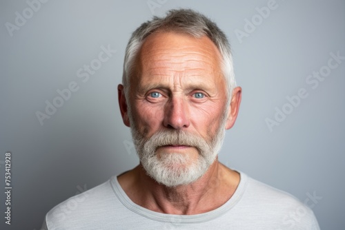 Portrait of a senior man with white beard and mustache looking surprised while standing against grey background