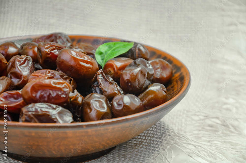 Fototapeta premium Dates in a brown plate on a textured light background, side view