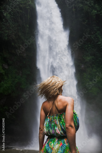 Luxurious blonde posing by a waterfall in a swimsuit  rear view.
