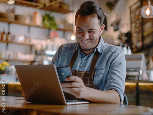 Smiling young man with laptop and smartphone in a modern cafe setting, embodying successful startup culture.