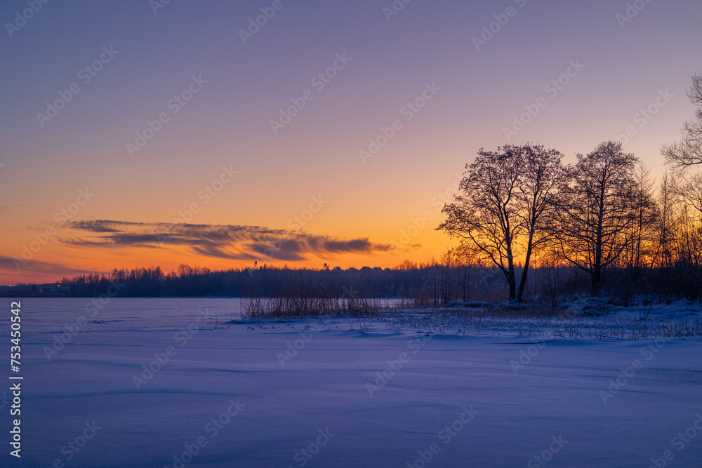 A beautiful winter sunrise scenery of frozen lake and forest. Colorful landscape with dawn skies in Northern Europe.