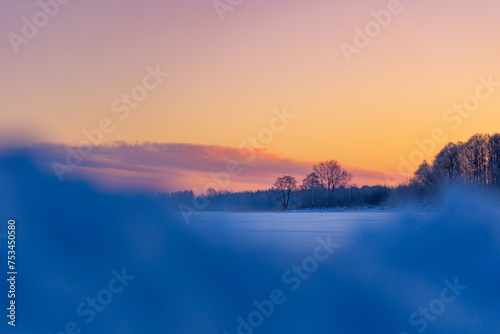 A beautiful winter sunrise scenery of frozen lake and forest. Colorful landscape with dawn skies in Northern Europe.