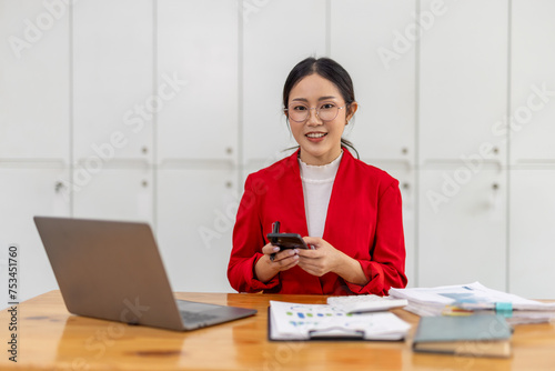 Shot of a young asian woman working using smart phone and notebook computer, woman using smart phone in interior, woman at her workplace using technology, flare light © David