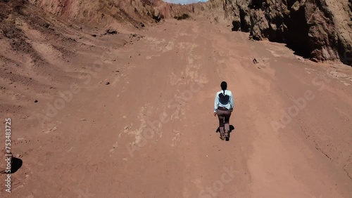 Aerial tilts up to woman walking alone in remote arid red rock canyon photo