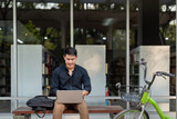 Asian businessman with bicycle using laptop and sitting outside the office building. man commuting on bike go to work. Eco friendly vehicle, sustainable lifestyle concept