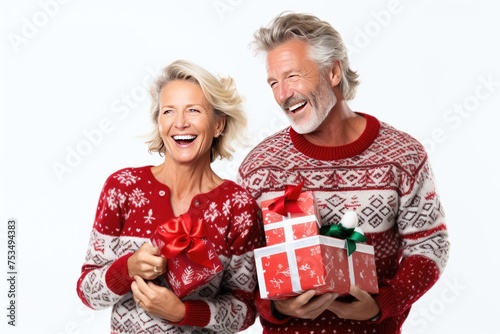 An elderly couple wearing Christmas sweaters, holding gift-wrapped presents and smiling photo